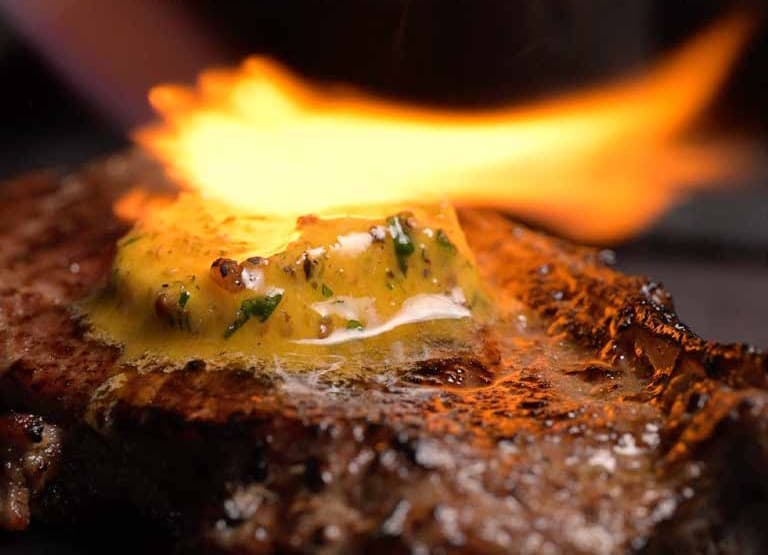 Earle’s compound butter being flamed over a charcoal-grilled steak